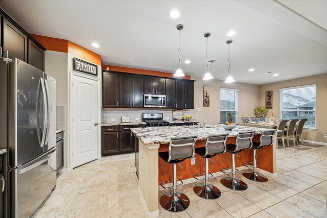 kitchen with decorative light fixtures, a kitchen breakfast bar, stainless steel appliances, dark brown cabinets, and a center island with sink