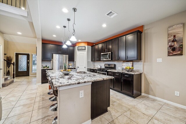 kitchen featuring pendant lighting, a breakfast bar, stainless steel appliances, light stone countertops, and an island with sink