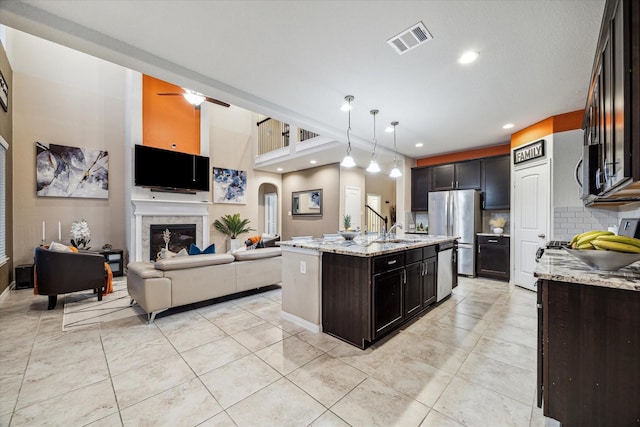 kitchen with tasteful backsplash, an island with sink, hanging light fixtures, light stone counters, and stainless steel appliances