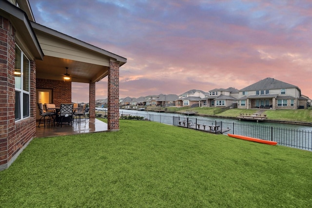 yard at dusk featuring a patio, a water view, and ceiling fan