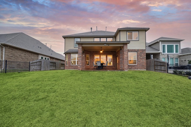 back house at dusk with a patio area and a lawn