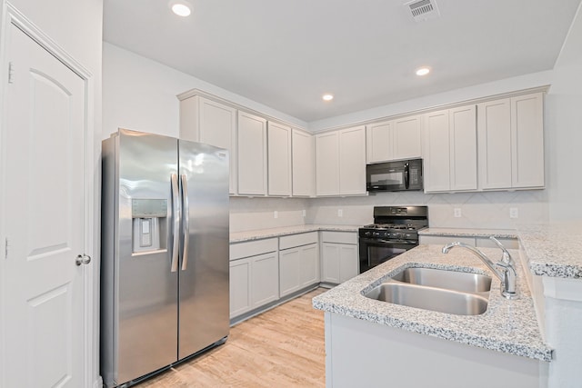 kitchen featuring decorative backsplash, light hardwood / wood-style floors, light stone counters, black appliances, and sink