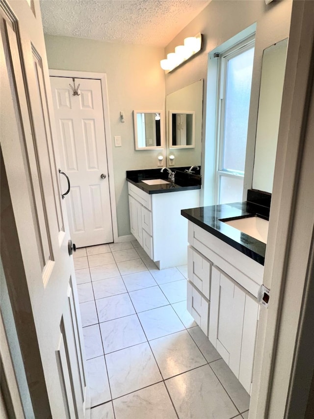 bathroom with a textured ceiling, two vanities, and a sink