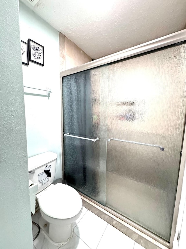 full bath featuring tile patterned flooring, a shower stall, toilet, and a textured ceiling