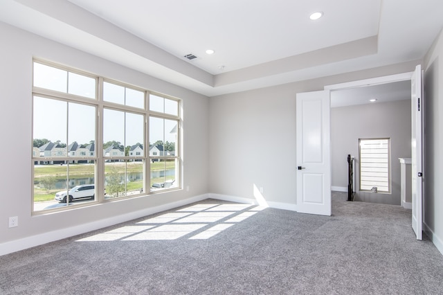 empty room with a water view, a raised ceiling, and carpet floors