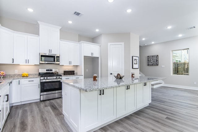 kitchen featuring light stone counters, a kitchen island, light hardwood / wood-style flooring, white cabinetry, and appliances with stainless steel finishes