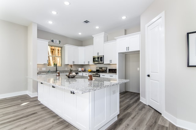 kitchen with light wood-type flooring, white cabinetry, appliances with stainless steel finishes, and light stone counters