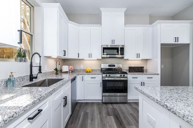 kitchen with white cabinets, sink, appliances with stainless steel finishes, light stone countertops, and dark hardwood / wood-style flooring