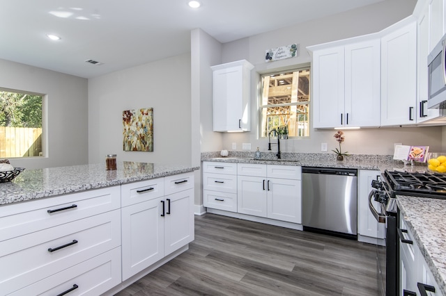 kitchen with sink, white cabinetry, stainless steel appliances, light stone countertops, and dark hardwood / wood-style flooring