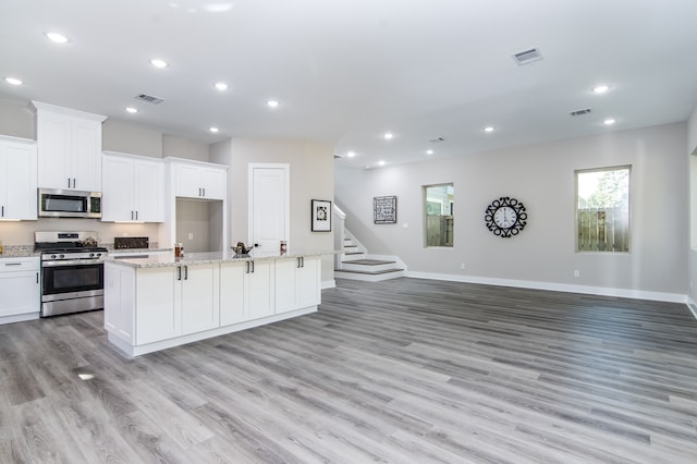 kitchen with light stone counters, a center island with sink, white cabinetry, stainless steel appliances, and light hardwood / wood-style floors