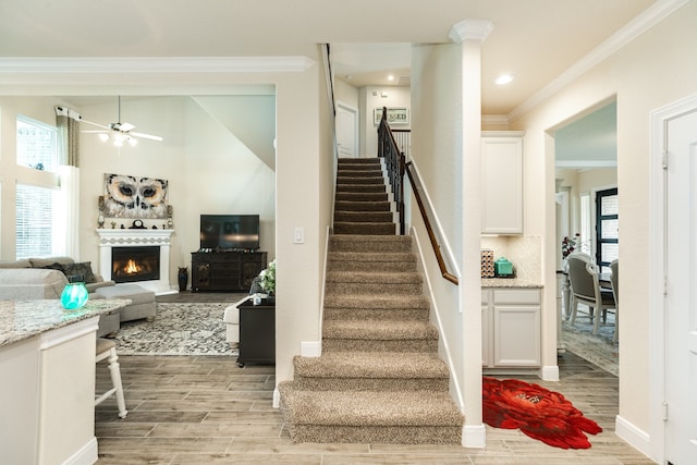 stairway with ceiling fan, decorative columns, crown molding, and hardwood / wood-style floors