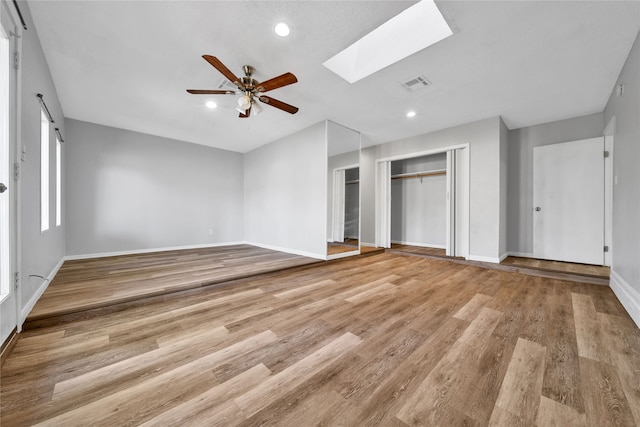 unfurnished living room featuring light hardwood / wood-style floors, a skylight, and ceiling fan