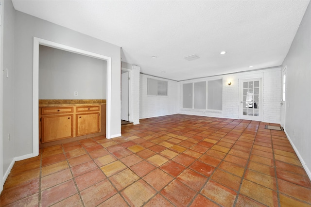 unfurnished living room with brick wall and a textured ceiling