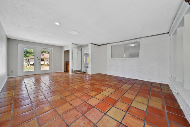 unfurnished living room featuring tile patterned flooring, a textured ceiling, brick wall, and french doors