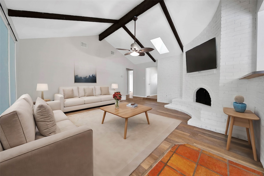 living room featuring beamed ceiling, hardwood / wood-style flooring, a fireplace, a skylight, and ceiling fan