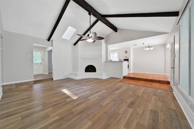 unfurnished living room with ceiling fan with notable chandelier, hardwood / wood-style floors, beamed ceiling, and a fireplace