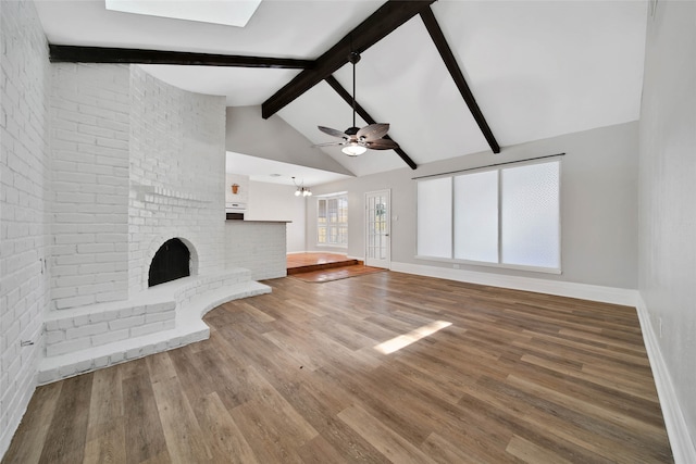 unfurnished living room with brick wall, a brick fireplace, beamed ceiling, ceiling fan, and hardwood / wood-style flooring