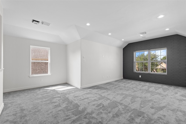 carpeted empty room featuring vaulted ceiling and brick wall