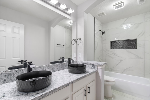 full bathroom with a textured ceiling, tiled shower / bath combo, vanity, and toilet