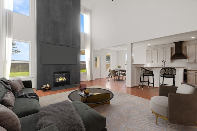 living room featuring a towering ceiling, light wood-type flooring, a fireplace, and sink