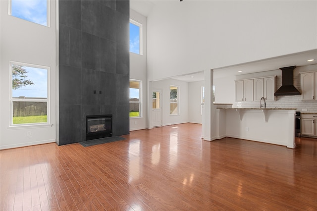 unfurnished living room with wood-type flooring, a fireplace, a towering ceiling, and sink