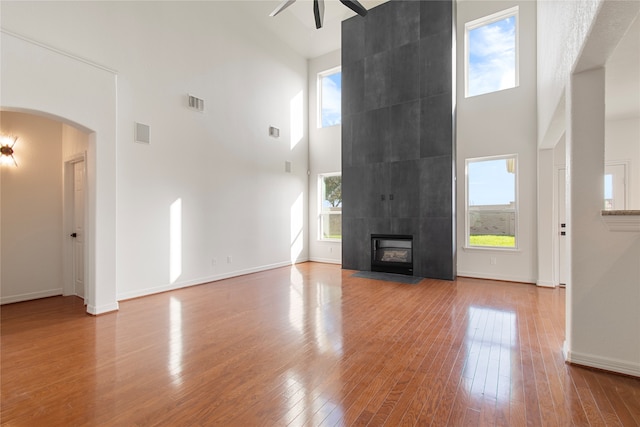 unfurnished living room with a towering ceiling, a tiled fireplace, and a wealth of natural light