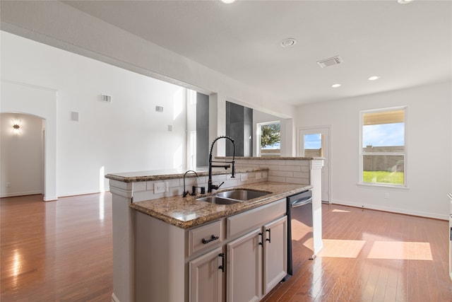 kitchen with a center island with sink, stainless steel dishwasher, sink, and a wealth of natural light