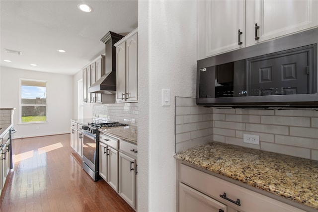 kitchen featuring light stone counters, wall chimney range hood, decorative backsplash, appliances with stainless steel finishes, and dark hardwood / wood-style flooring