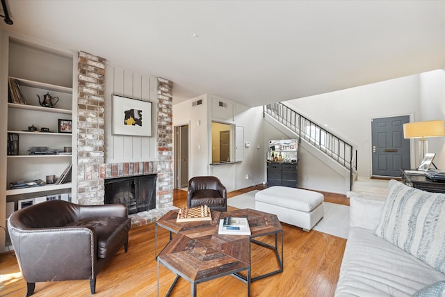 living room with a brick fireplace, light wood-type flooring, and built in features