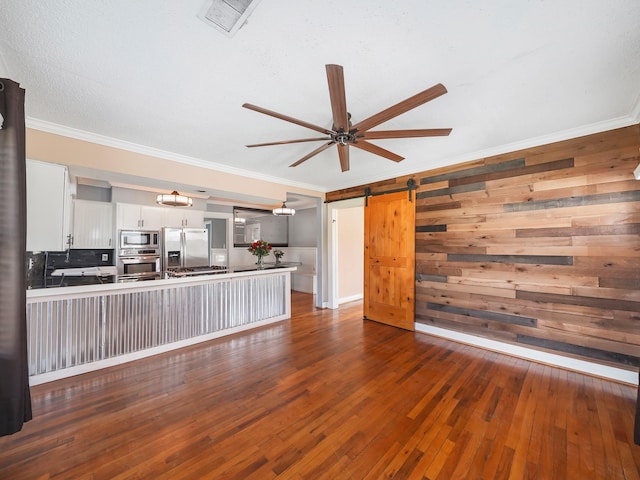 unfurnished living room featuring dark wood finished floors, a barn door, ornamental molding, ceiling fan, and visible vents