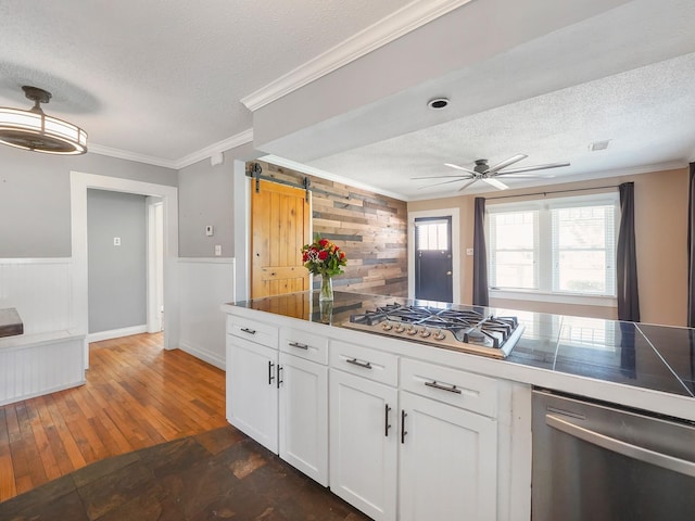 kitchen with stainless steel appliances, ceiling fan, white cabinetry, ornamental molding, and a textured ceiling