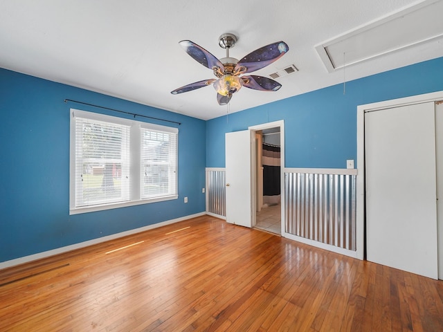 unfurnished bedroom with hardwood / wood-style floors, a closet, attic access, visible vents, and a ceiling fan
