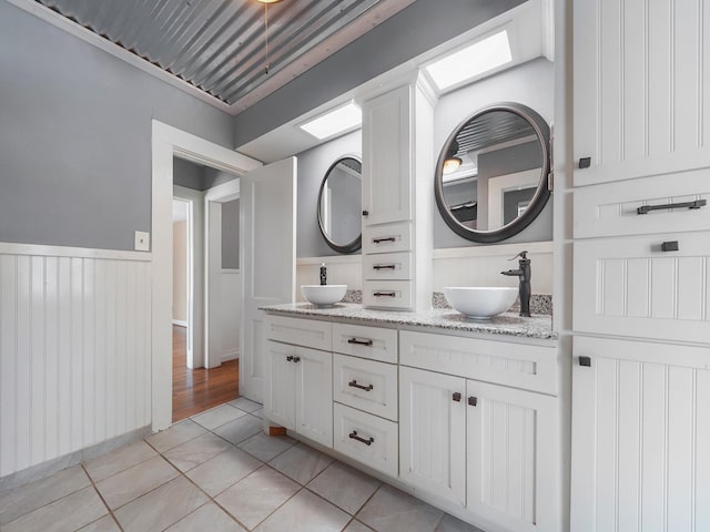 full bathroom with tile patterned floors, a wainscoted wall, double vanity, and a sink