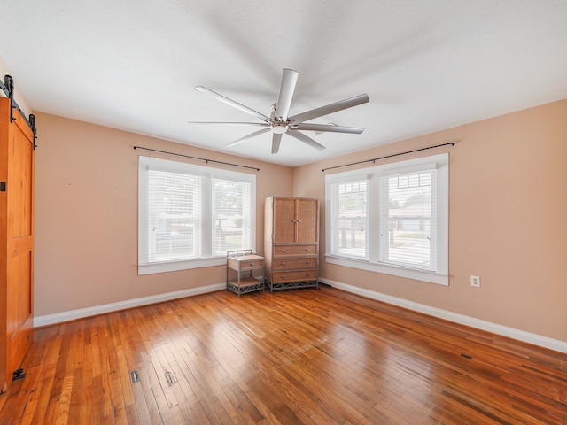 interior space featuring a barn door, wood-type flooring, a textured ceiling, and ceiling fan