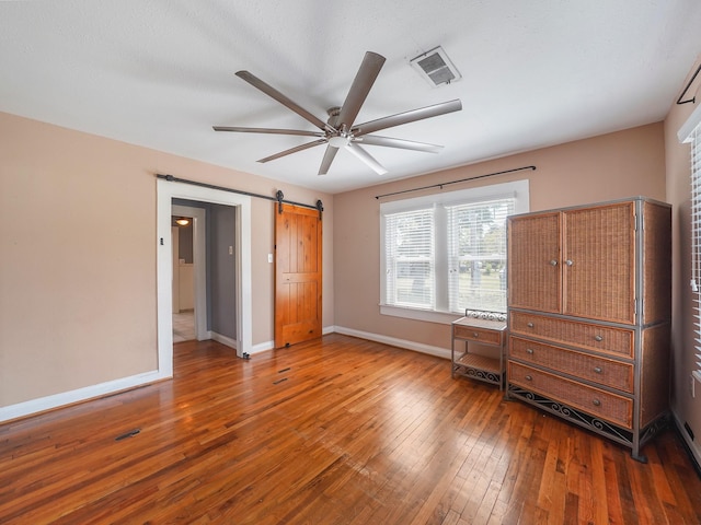 unfurnished bedroom with hardwood / wood-style floors, a barn door, baseboards, visible vents, and a ceiling fan