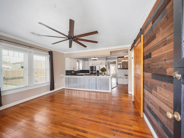 unfurnished living room with ornamental molding, sink, a textured ceiling, hardwood / wood-style flooring, and a barn door