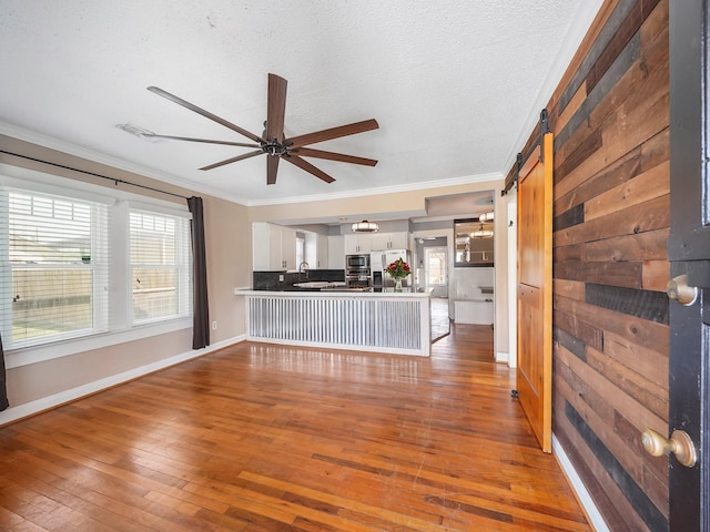 unfurnished living room featuring ornamental molding, a ceiling fan, hardwood / wood-style floors, and a barn door
