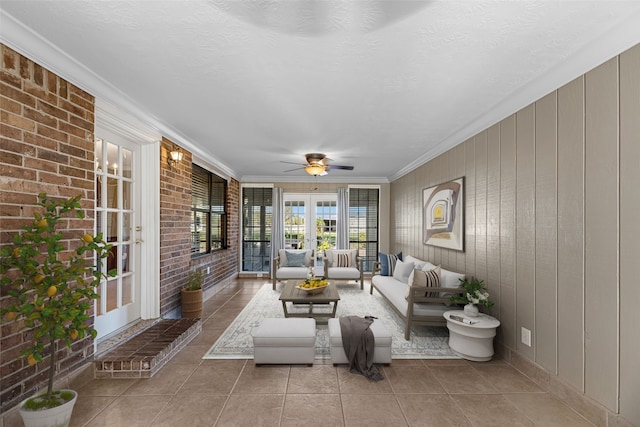 living room with french doors, light tile patterned floors, ornamental molding, and brick wall