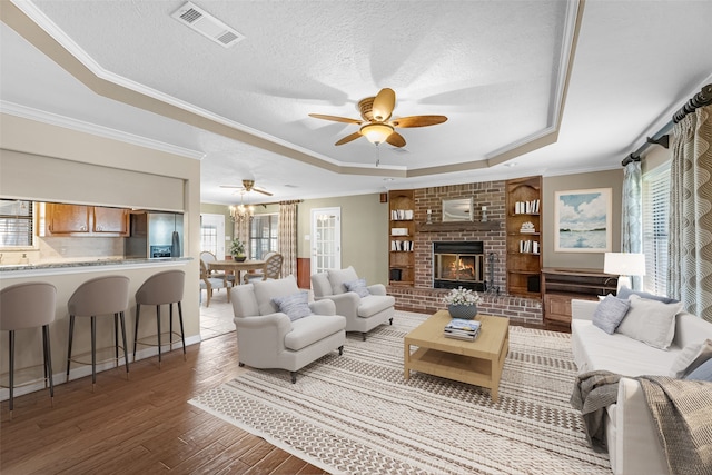 living room with wood-type flooring, a tray ceiling, a brick fireplace, and a wealth of natural light