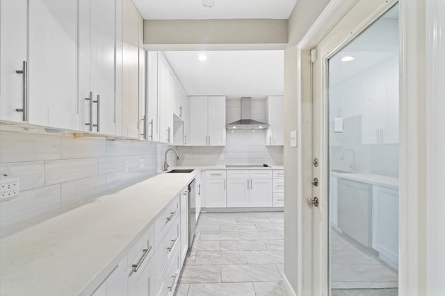 kitchen with backsplash, white cabinetry, sink, and wall chimney range hood