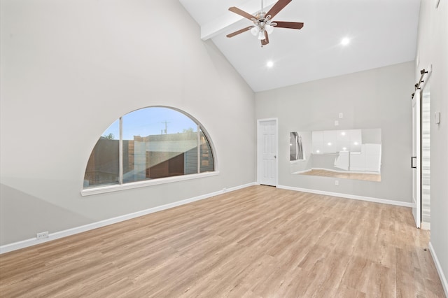 unfurnished living room with light hardwood / wood-style floors, beam ceiling, a barn door, high vaulted ceiling, and ceiling fan