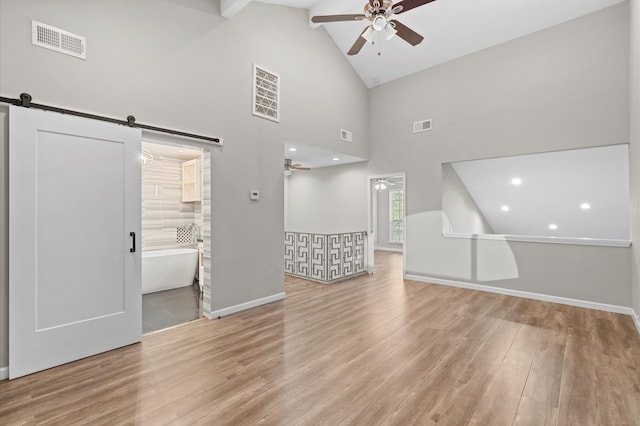 interior space with high vaulted ceiling, light wood-type flooring, ceiling fan, and a barn door