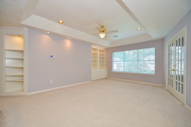 carpeted spare room with french doors, ceiling fan, a raised ceiling, and built in features