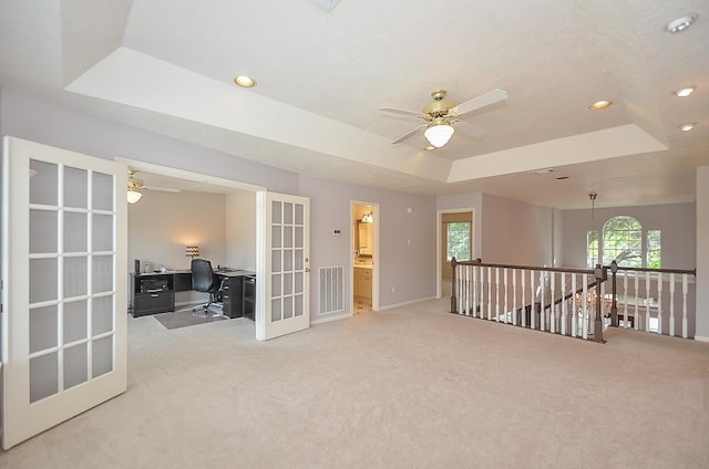 spare room featuring french doors, carpet flooring, ceiling fan with notable chandelier, and a raised ceiling