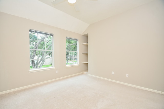 carpeted empty room with vaulted ceiling, built in shelves, and ceiling fan