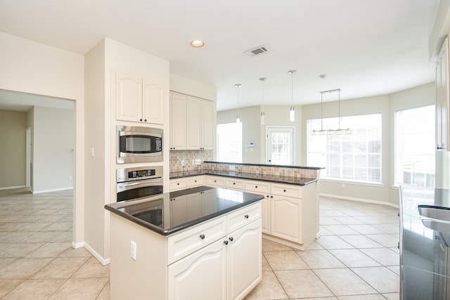 kitchen with tasteful backsplash, appliances with stainless steel finishes, kitchen peninsula, hanging light fixtures, and white cabinets