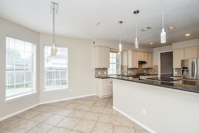 kitchen with tasteful backsplash, sink, stainless steel fridge, pendant lighting, and light tile patterned floors