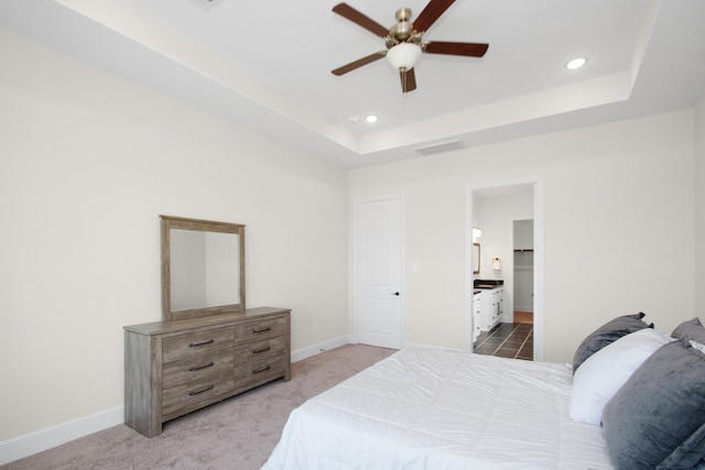 bedroom featuring ensuite bath, carpet floors, a tray ceiling, and ceiling fan