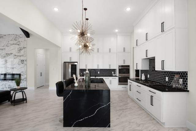 kitchen with a kitchen island with sink, hanging light fixtures, stainless steel appliances, a chandelier, and tasteful backsplash