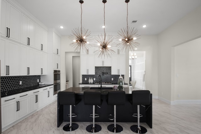 kitchen with sink, an island with sink, stainless steel double oven, pendant lighting, and an inviting chandelier